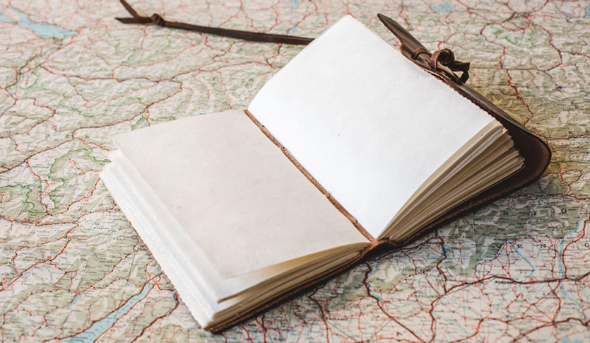 An open blank notebook sitting on top of a map.